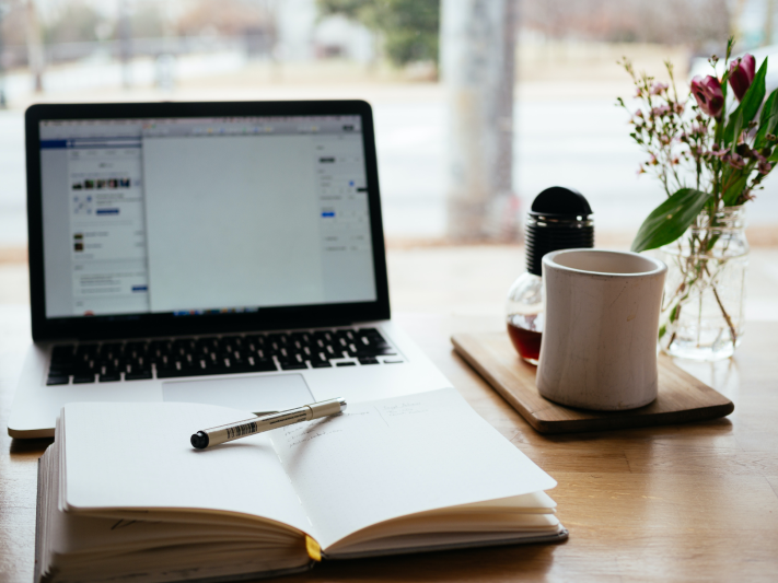 A desk with an open laptop, an open notebook, and a coffee mug